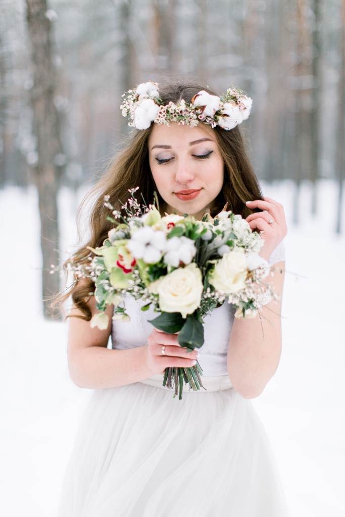 Eine junge Braut mit einem Blumenstrauß in einem winterlich verschneiten Wald
