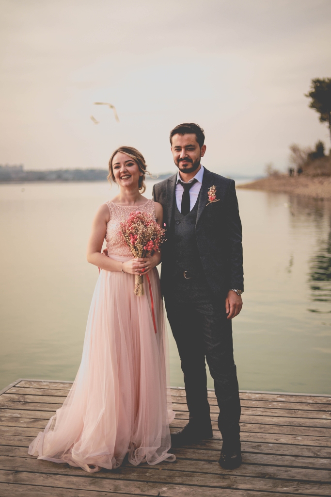 Braut mit rosa Brautkleid und Bräutigam im Anzug auf einem Steg